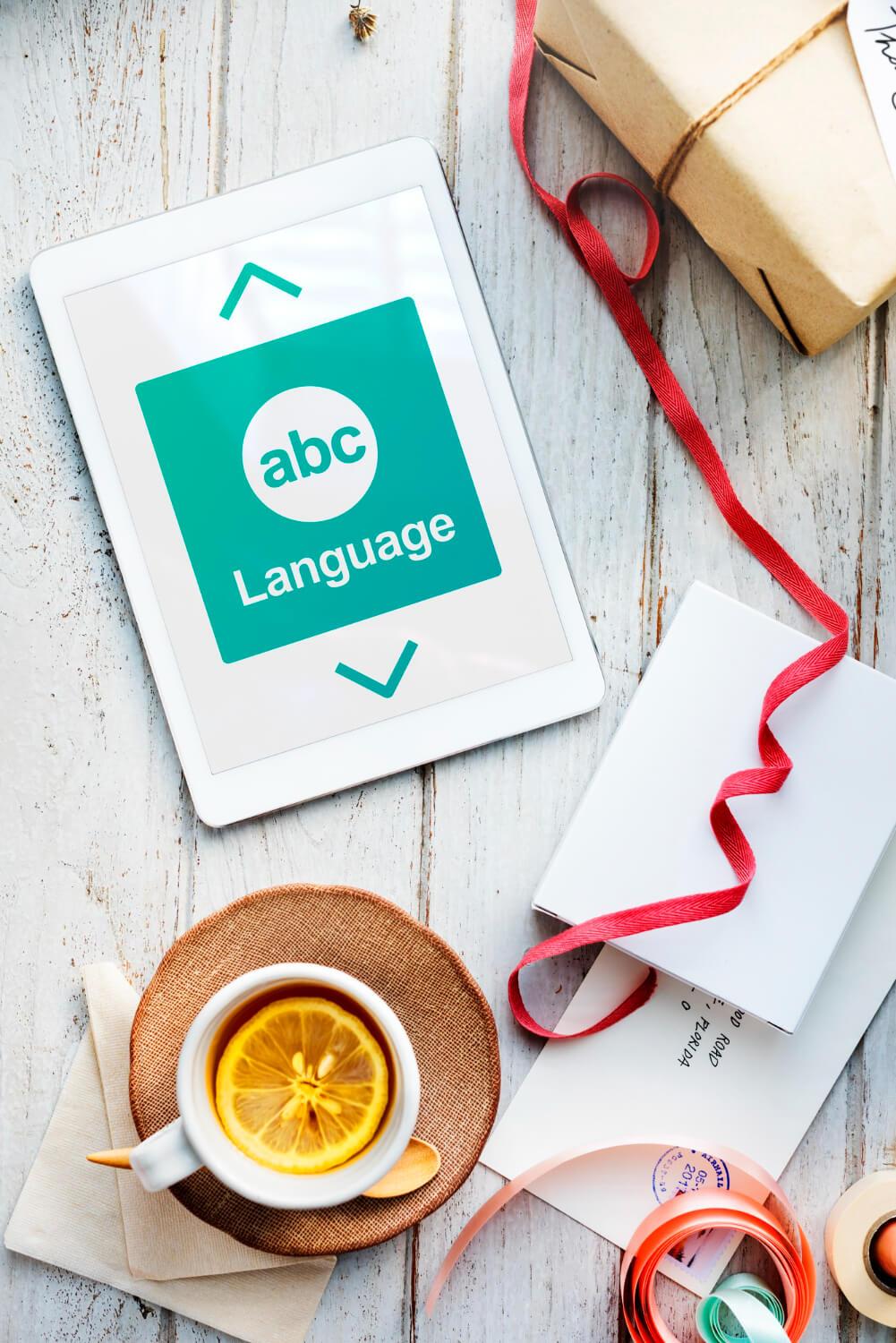 Digital tablet displaying 'abc Language' over a rustic wooden table, surrounded by a cup of lemon tea, a wrapped gift box, and ribbon, symbolizing global communication and professional Chinese translation services.